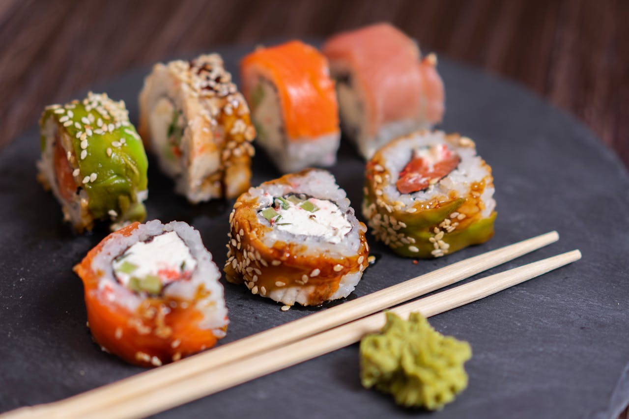A close-up view of a colorful sushi platter with wasabi and chopsticks on a slate board.