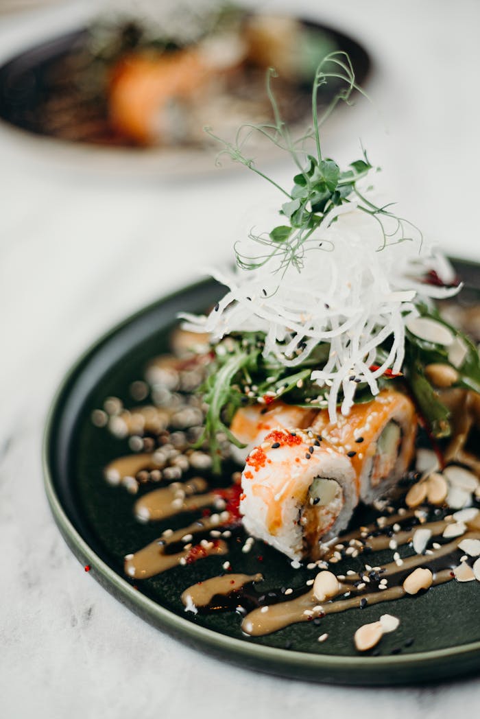 Close-up of a gourmet sushi roll elegantly presented with fresh garnishes and sauce drizzles on a dark plate.